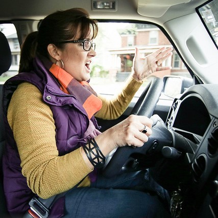 A woman shouts and makes an aggressive hand gesture as she drives her car. A woman shouts and makes an aggressive hand gesture as she drives her car.
