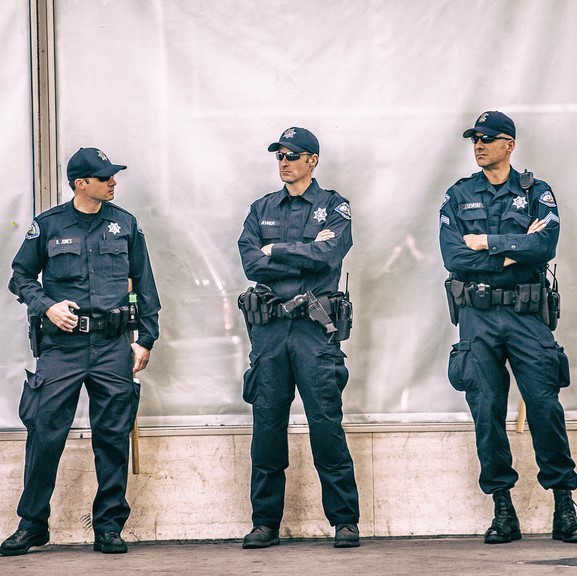 A group of uniformed police officers stand together on the sidewalk. A group of uniformed police officers stand together on the sidewalk.
