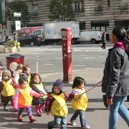 A group of preschool students are lead along a city street by an adult. A group of preschool students are lead along a city street by an adult.