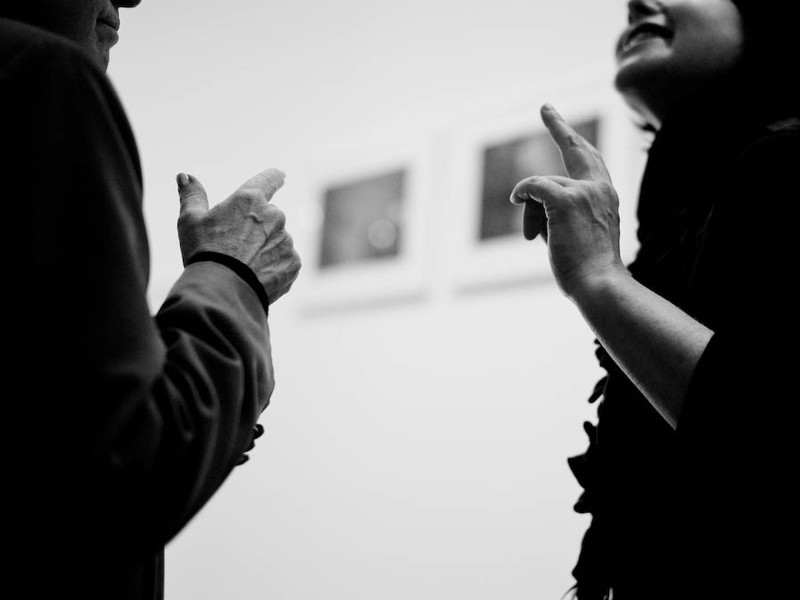 A man and woman are engaged in conversation and making identical hand movements. A man and woman are engaged in conversation and making identical hand movements.