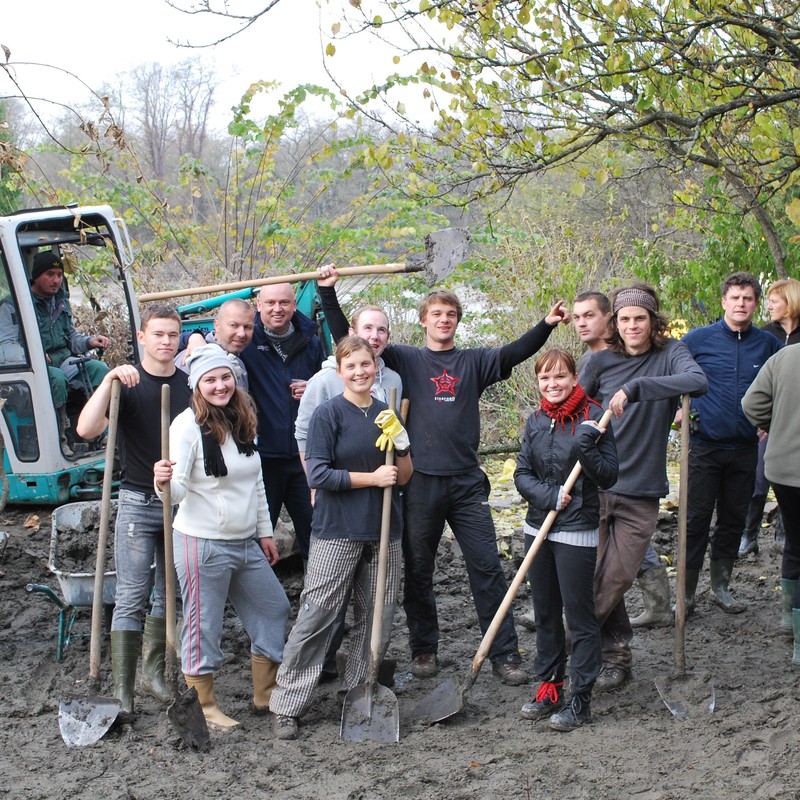 A group of men and women stand together in a muddy field with shovels and wheelbarrows as they participate in an outdoor volunteer project. A group of men and women stand together in a muddy field with shovels and wheelbarrows as they participate in an outdoor volunteer project.
