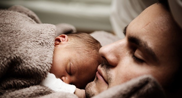 A father sleeps with an infant asleep on his chest. A father sleeps with an infant asleep on his chest.