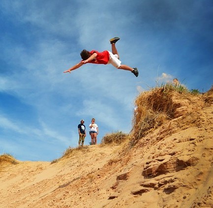 A young man jumps head first off the top of a sand dune and down a steep slope. A young man jumps head first off the top of a sand dune and down a steep slope.