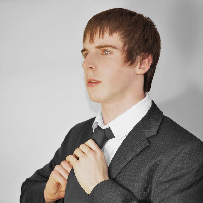 A young man in a suit adjusts his tie. A young man in a suit adjusts his tie.